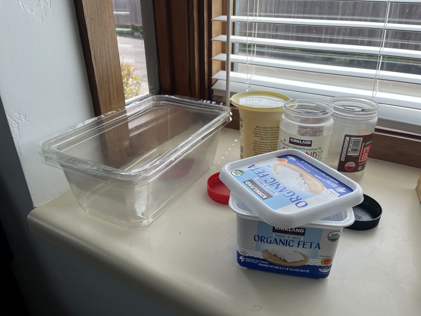 A washed deli tub, an empty feta container and two nut butter jars drying on a windowsill
